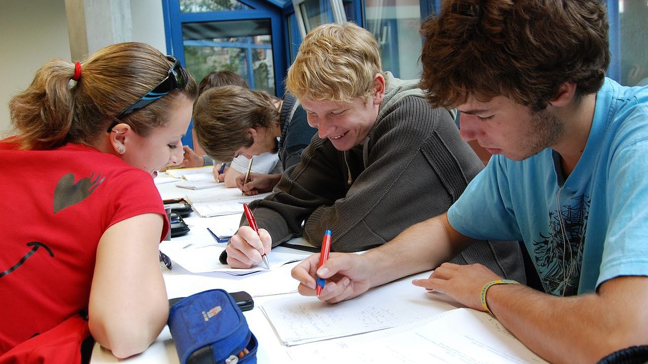 Schüler*innen sitzen am Tisch zusammen und knobeln an mathematischen Aufgaben