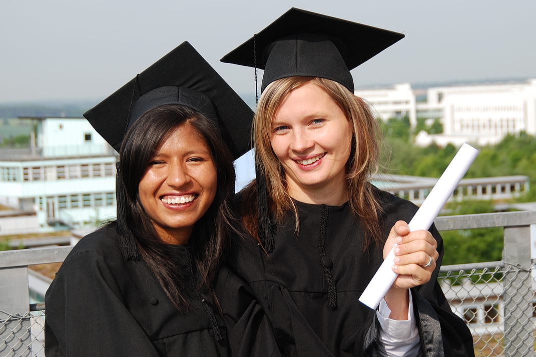 Studierende unterschiedlicher Herkunft mit Talar und Abschlusszeugnis