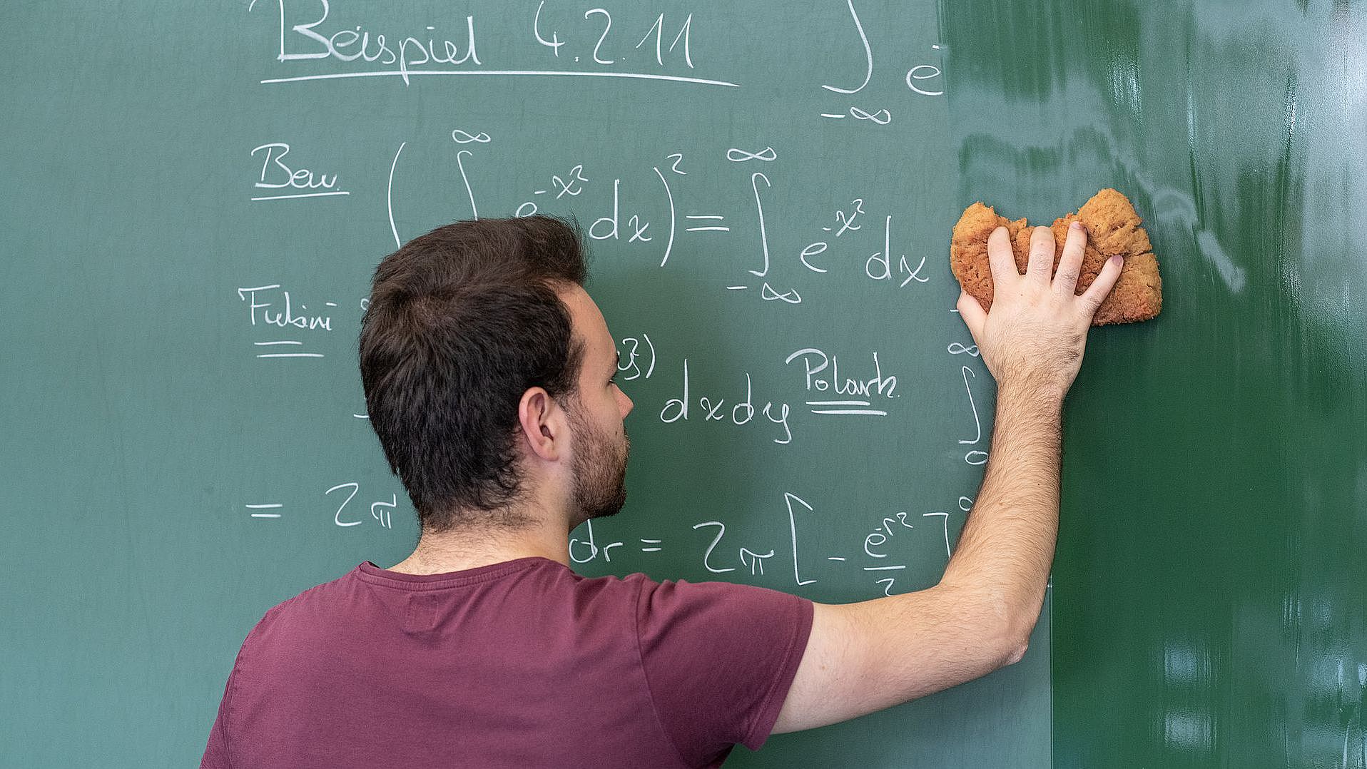 [Translate to english:] Dozent wischt die Tafel auf der mathematische Formeln stehen