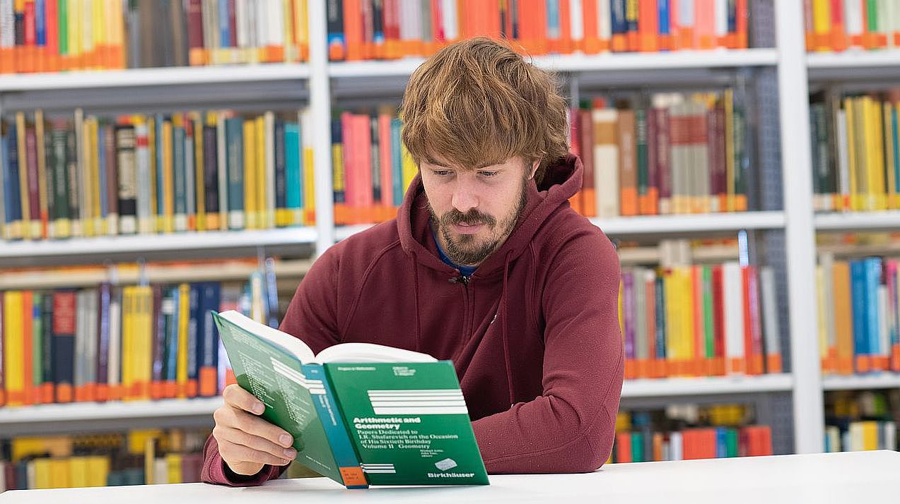 Student sitzt in der Bin und liest ein mathematisches Buch