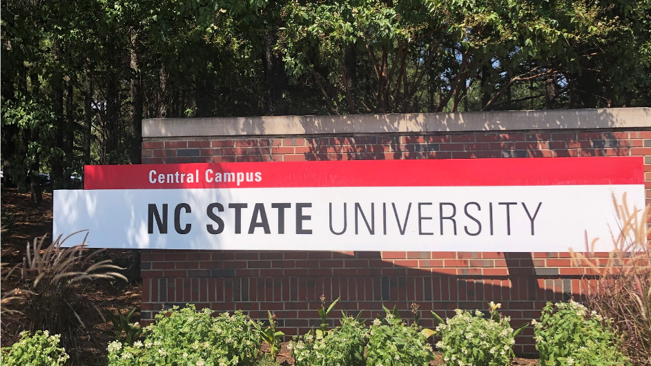 NC State University auf einem Banner vor einer Mauer der Universität