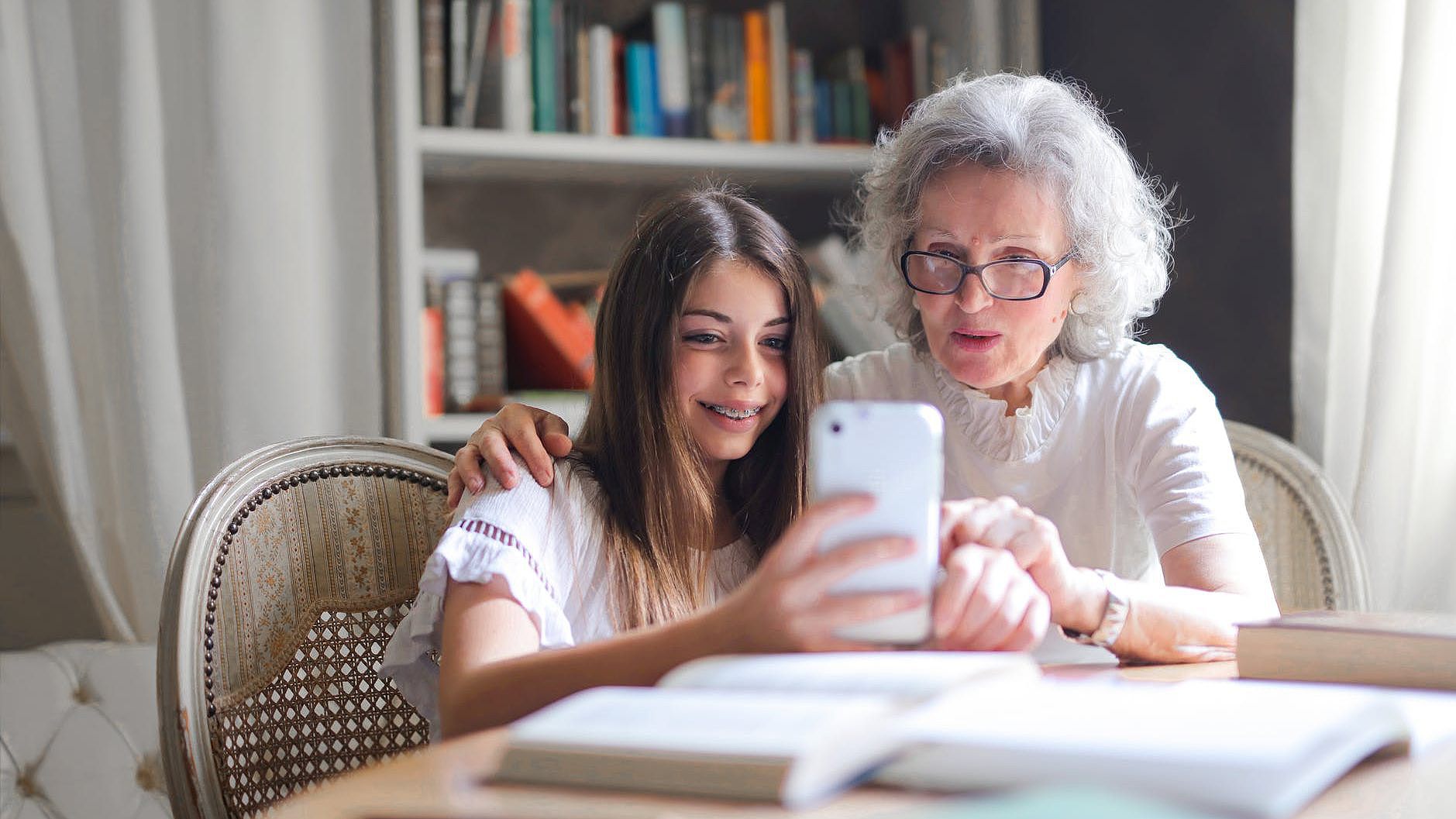 Seniorin und Jugendliche sitzen gemeinsam vor einem Mobiltelefon