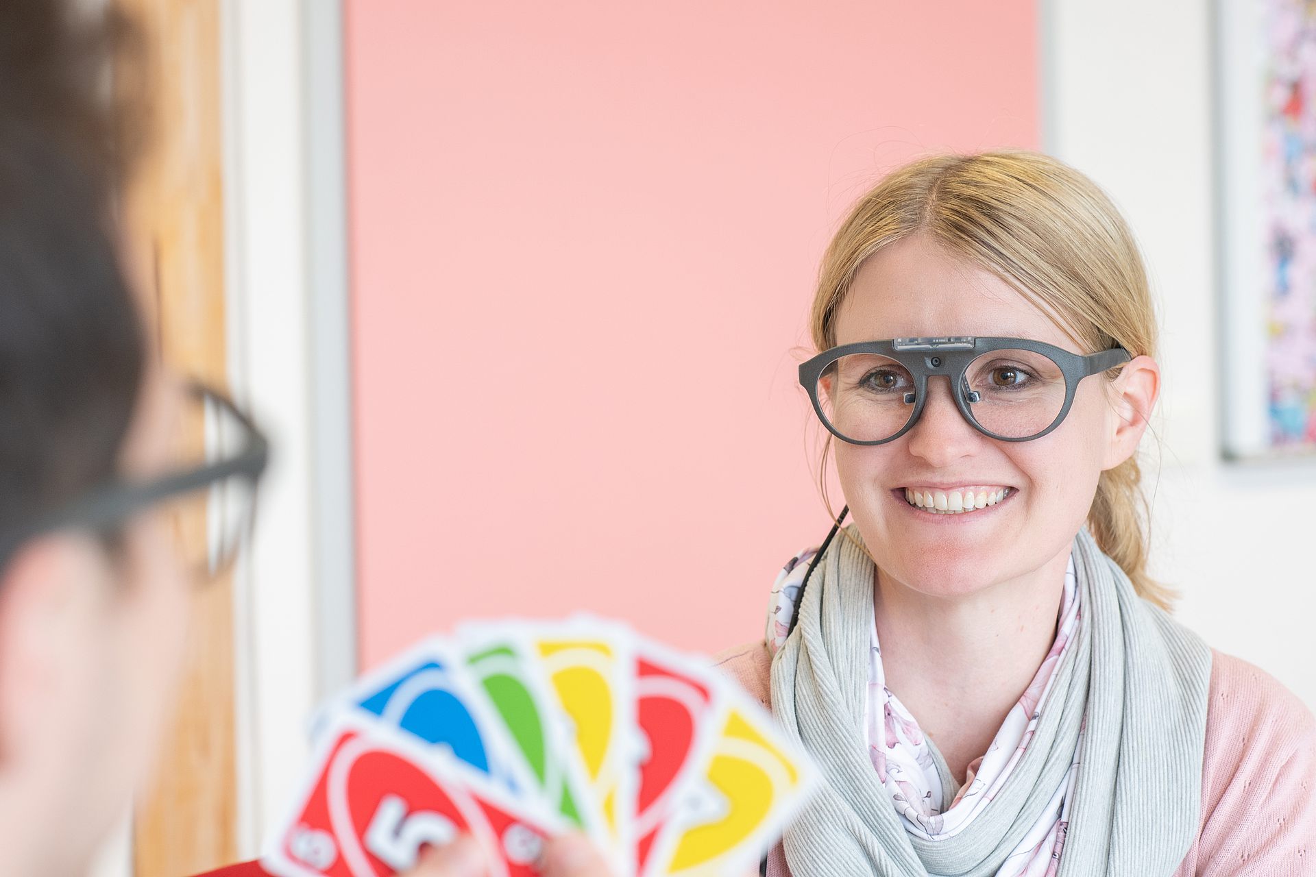 Foto von einer Person mit mobilem Eyetracker; im Vordergrund sitzt ihr gegenüber eine Person, die Spielkarten hochhält