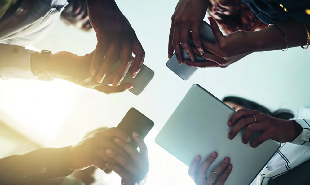 Foto von unten; darauf vier zusammenstehenden Personen, die jeweils ein Smartphone oder ein Tablet in den Händen haben